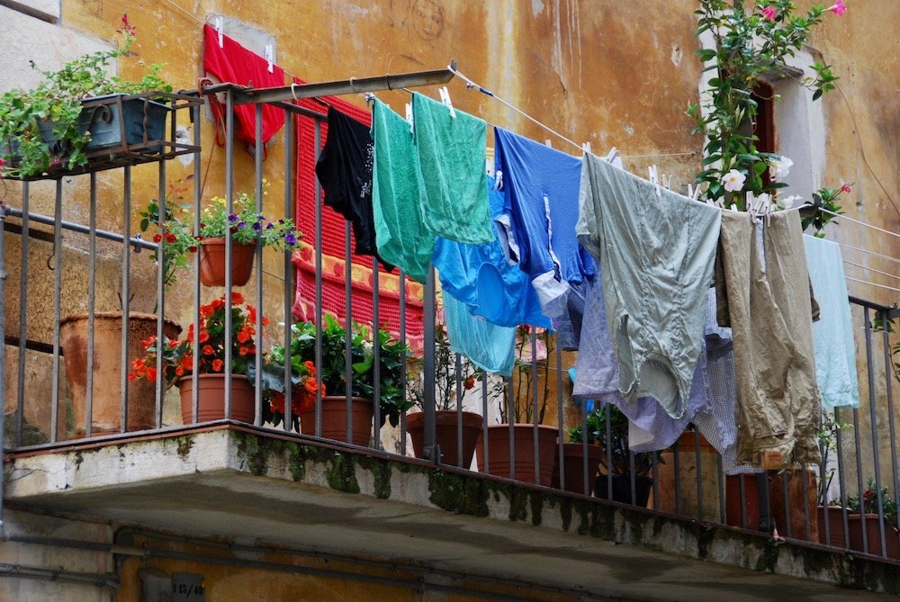 Typisch Italiaans straatbeeld in Maratea: kleurrijk wasgoed aan de lijn en bloeiende planten op een balkon in de historische binnenstad.