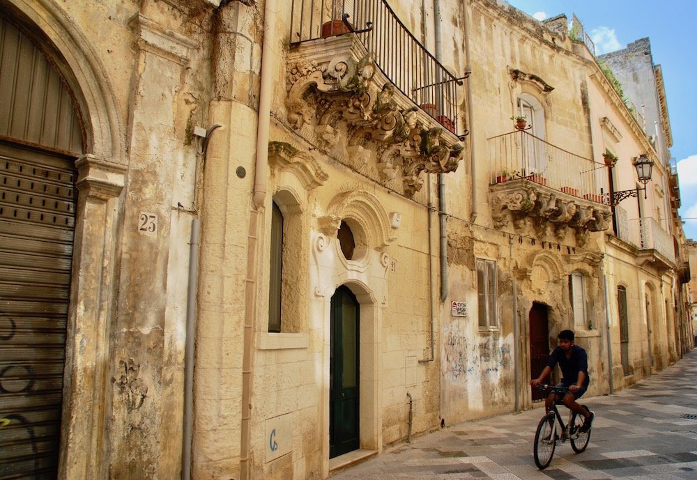 Jongen fietst door een sfeervolle zandkleurige straat in het historische centrum van Lecce, Italië
