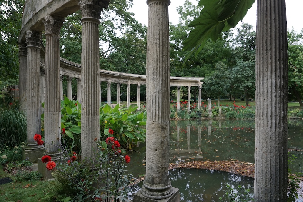 Groen park met slingerende paden, hoge bomen en een klassieke zuilengalerij in Parc Monceau in Parijs